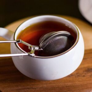 Closeup of a tea infuser in a cup of black tea.